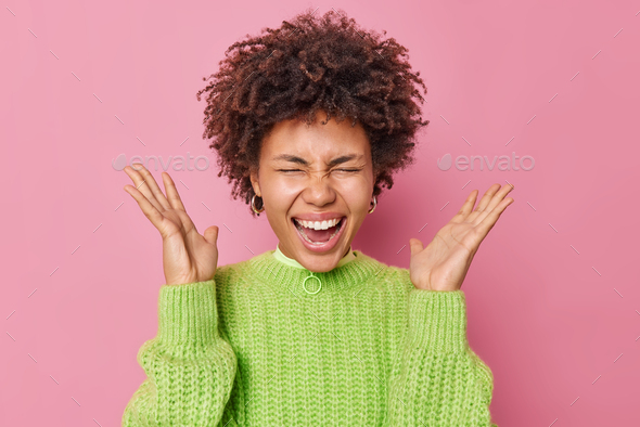 Indoor Shot Of Emotional Curly Haired Young Woman Screams Loudly Keeps